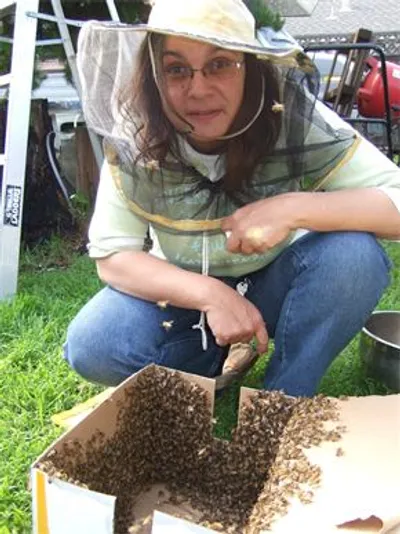 Ella in a beekeeping veil tending a box of bees on the grass