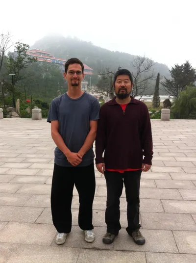 Standing beside an older Chinese man on a plaza below a mist-covered mountain