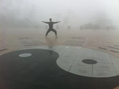 A person in a wide stance with arms extended on a yin-yang plaza shrouded in mist