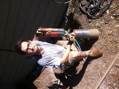 Operating a handheld core drill against a wall over a freshly dug trench