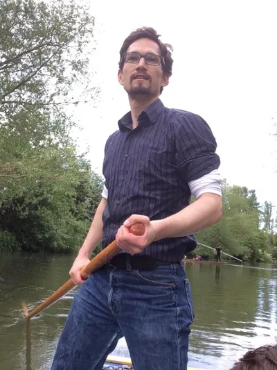 Punting a flat-bottomed boat along a tree-lined river