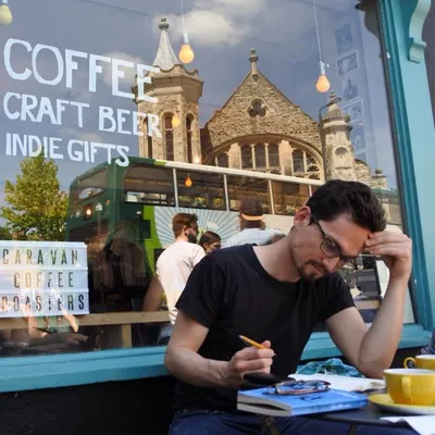 Writing in a notebook at an outdoor table outside Caravan Coffee Roasters