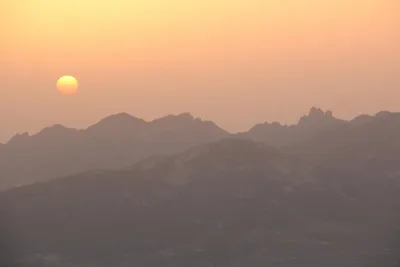 The sun setting over layered, hazy mountain ridges
