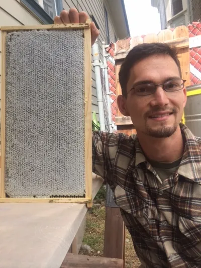 A beekeeper smiling while holding up a frame of fully capped honeycomb